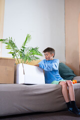 Boy unpacking boxes in new home putting houseplant on sofa
