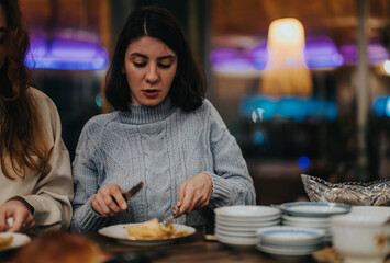 A young woman dressed warmly enjoys a meal at a beautifully lit restaurant setting, surrounded by cozy decor.