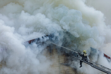 Firefighter on Ladder Fighting Intense Blaze with Heavy Smoke During Emergency Rescue Operation