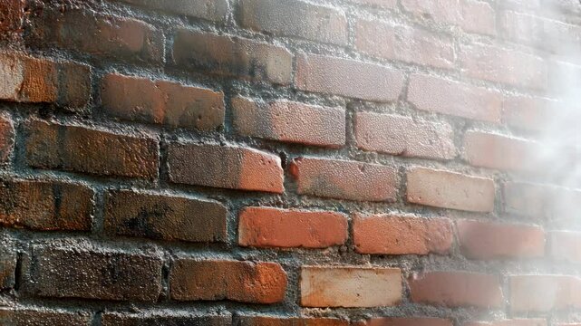 Pressure washing a brick wall. Intense spray removes dirt and grime. Contrasting clean and dirty sections highlight the cleaning process. Outdoor maintenance.