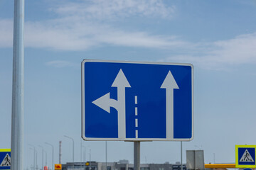 A road sign displays arrows pointing straight and left, guiding drivers at an intersection under a...
