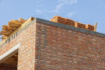 Workers are busy constructing a brick building, stacking wooden materials on the roof against a...