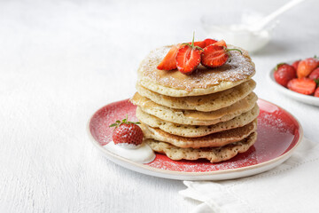 Stack of homemade pancakes with fresh strawberries and powdered sugar on plate, served with yogurt,...