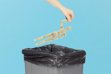 Throw wooden man, in the trash, outstretched hand with wooden mannequin in front of trash can