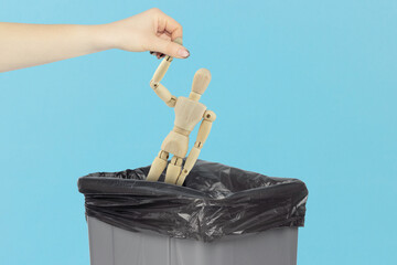 Throw wooden man, in the trash, outstretched hand with wooden mannequin in front of trash can