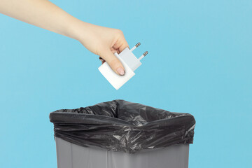 Throw network charger for phone in trash, outstretched hand with network charger for phone in front of trash can. Concept of using original devices