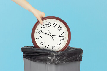 Throw round wall clock in the trash, outstretched hand with round wall clock in front of trash can