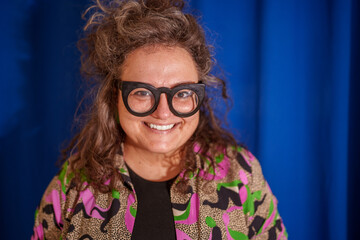 Smiling female designer in vibrant shirt and glasses, radiating creativity against blue backdrop