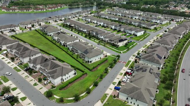 Luxury row of houses near lake in suburb neighborhood of Orlando, Florida. Aerial wide shot. White apartment houses with grey roof in modern style. Upscale housing area of American city.