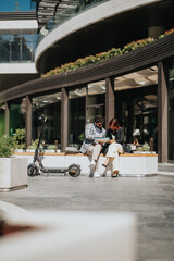 Two people collaborate outdoors on a project while sitting near an electric scooter.