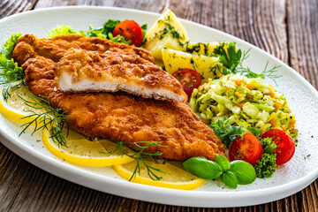 Crispy breaded chicken cutlets with boiled potatoes and young cabbage salad on wooden table	