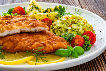 Crispy breaded chicken cutlets with boiled potatoes and young cabbage salad on wooden table	