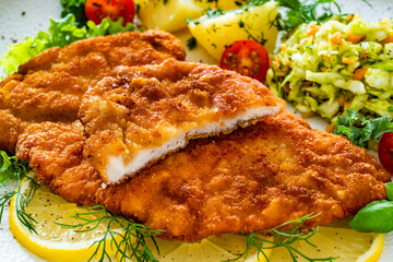 Crispy breaded chicken cutlets with boiled potatoes and young cabbage salad on wooden table	