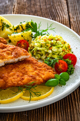 Crispy breaded chicken cutlets with boiled potatoes and young cabbage salad on wooden table	