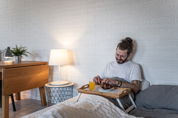 Smiling freelancer enjoying breakfast in bed while working from home