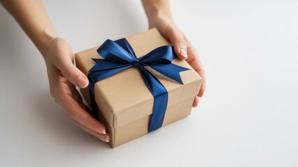 Hands holding a simple kraft paper gift box tied with a luxurious blue satin ribbon