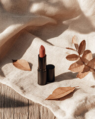 Lipstick placed on textured surface with dried leaves, creating warm and inviting atmosphere. soft colors and natural elements evoke sense of calm and beauty