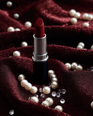 Vibrant red lipstick elegantly placed on rich burgundy fabric, surrounded by lustrous white pearls and sparkling small diamonds, creating luxurious and glamorous atmosphere