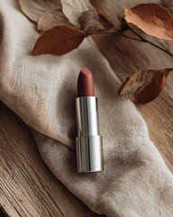 Beautiful lipstick sits elegantly on natural fabric, surrounded by dried leaves, creating warm and inviting atmosphere. rich color of lipstick complements earthy tones of setting