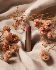 Beautiful lipstick sits elegantly soft beige linen background, surrounded by delicate dried flowers, creating warm and inviting atmosphere. combination of colors and textures evokes sense