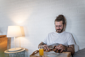 Young man enjoying breakfast in bed with pastry and orange juice