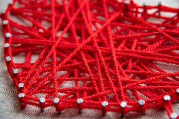 Creative use of vibrant red yarn intertwined around nails forms string art, showcasing textures and...
