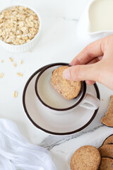 Hand is dipping breakfast cookie in a cup of oat milk. Top view.