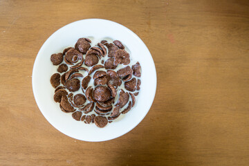 Chocolate cornflake with fresh milk in the ceramic white bowl on the wooden table