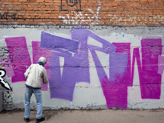 A guy paints graffiti with a spray can of purple paint.