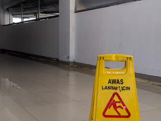 Yellow safety sign in Indonesian "AWAS LANTAI LICIN" (Caution Wet Floor) with a red falling figure symbol, indicating a slip hazard on a wet tiled floor in Banjarsari, West Java, Indonesia.