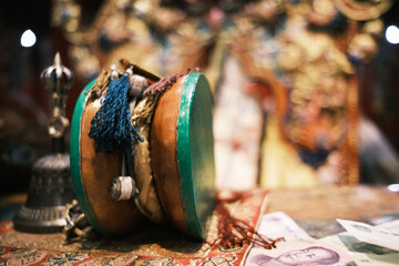 A close-up of a traditional Tibetan damaru drum with colorful tassels, placed beside a ritual bell...