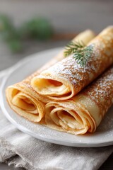 Delicious rolled pancakes topped with powdered sugar and greenery on a rustic plate