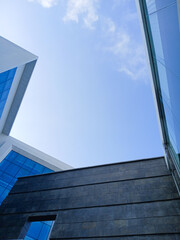 Modern glass building facade from a low-angle view against a bright blue sky with clouds....