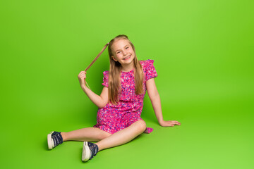 Smiling young girl in a pink dress sitting on green background highlighting cheerful mood and...