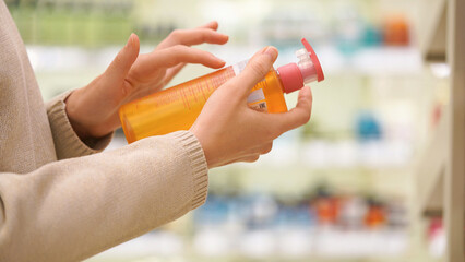 Woman holding a bottle of shampoo or body wash in a beauty store, reading the label, examining...