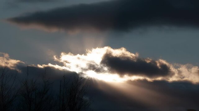 Sunset rays breaking through dramatic clouds over peaceful landscape