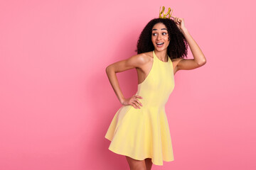 Happy young woman celebrates with a golden crown, wearing a stylish yellow dress against a vibrant...