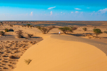 Scenic view man walking on a sand dune against blue sky at North Horr Sand dunes in Marsabit County, Kenya 
