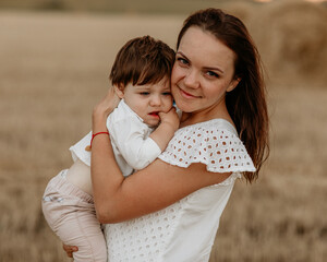 Mother with little son in her arms in a field of haystacks at sunset in summer