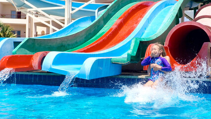 Children have fun sliding down Bright and colorful water slides in a clear blue pool on a sunny day...