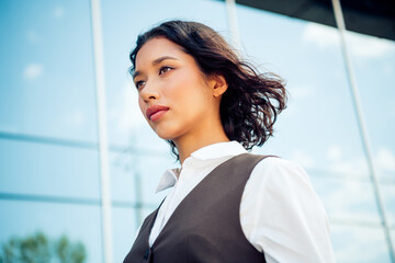 Portrait of a confident asian businesswoman in modern urban setting with clear blue sky in...