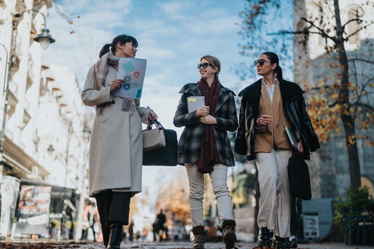Diverse businesswomen conversing while walking outdoors on a sunny urban day. They appear collaborative and engaged, creating an impression of teamwork, professionalism, and modern-day work dynamics.
