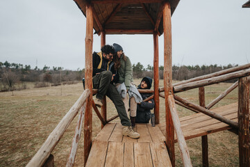 Friends spend quality time together outdoors, seated on a rustic wooden structure, surrounded by...