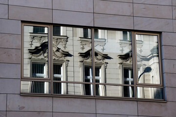 Ornate classical building facade reflected in modern glass windows. Decorative sculptures, columns,...