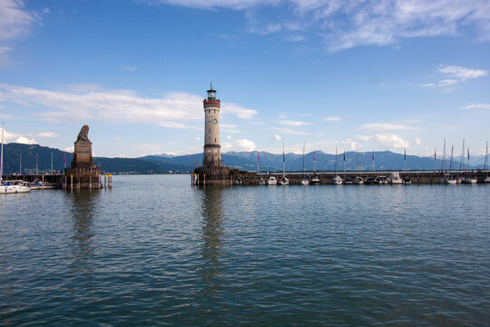 A wide-angle view of the iconic harbor entrance of Lindau on Lake Constance (Bodensee), under a bright blue sky with scattered clouds