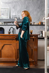 Elegant mature woman in teal velvet suit sitting at bar counter with cup of coffee in hand...