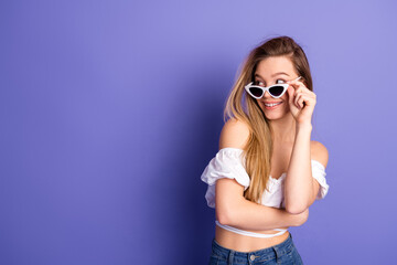 Obraz premium Joyful young woman wearing white sunglass posing over purple background, exuding happiness and confidence with stylish attire