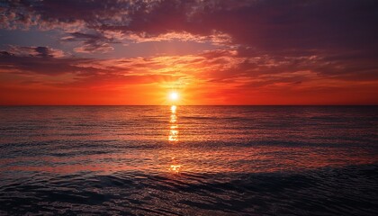 Obraz premium vivid red sunset over calm ocean waters with sun s reflection creating a serene and tranquil seascape during evening