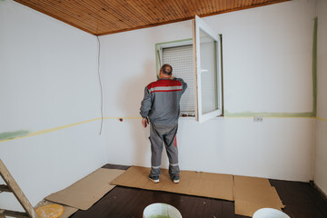 A worker wearing work clothing is making improvements to a room by managing the walls and checking...