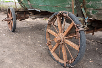 A close-up shot of the front wheel and side of an old, weathered wooden cart with peeling green...